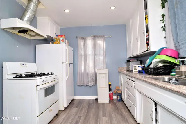 a kitchen with granite countertop a sink dishwasher stove and white cabinets with wooden floor