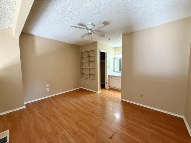 a view of an empty room with wooden floor and a ceiling fan