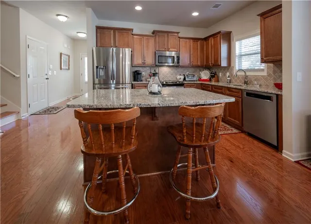 a kitchen with stainless steel appliances granite countertop a sink dishwasher a refrigerator and a stove with wooden floor