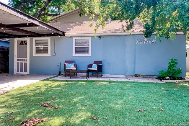 a backyard of a house with table and chairs plants and large tree