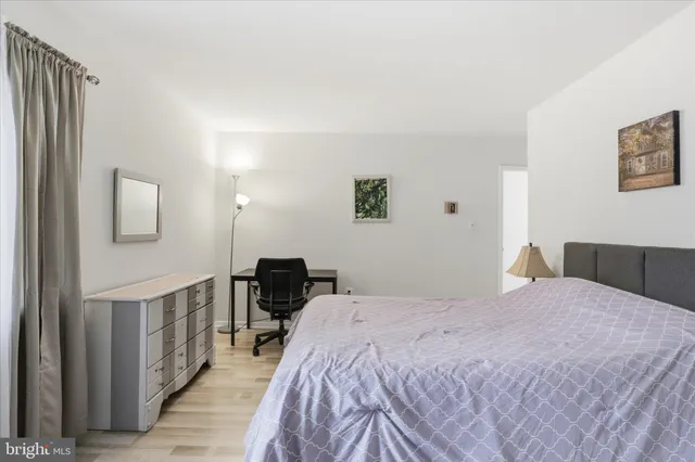 a bedroom with a bed a desk and chair with wooden floor