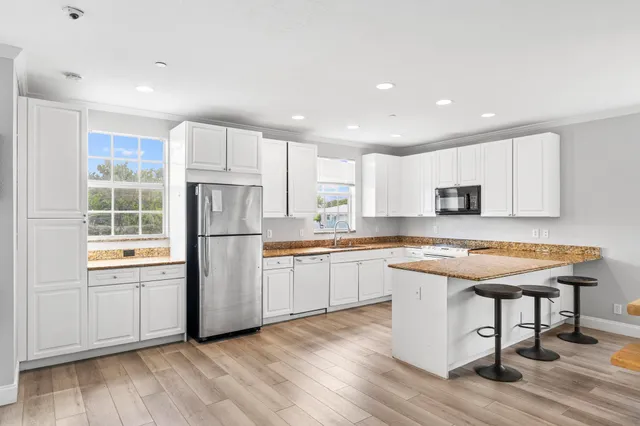 a kitchen with stainless steel appliances granite countertop a stove a sink dishwasher a refrigerator and white cabinets with wooden floor