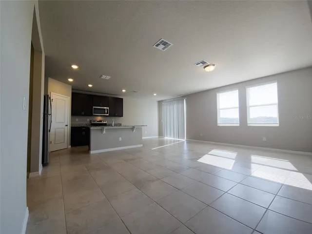 a view of an empty room with kitchen and window