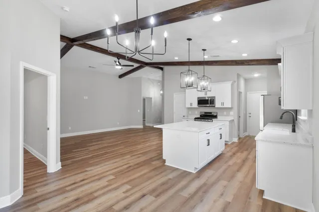 a large white kitchen with stainless steel appliances kitchen island granite countertop a refrigerator and a stove top oven