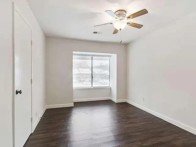 an empty room with wooden floor chandelier fan and windows