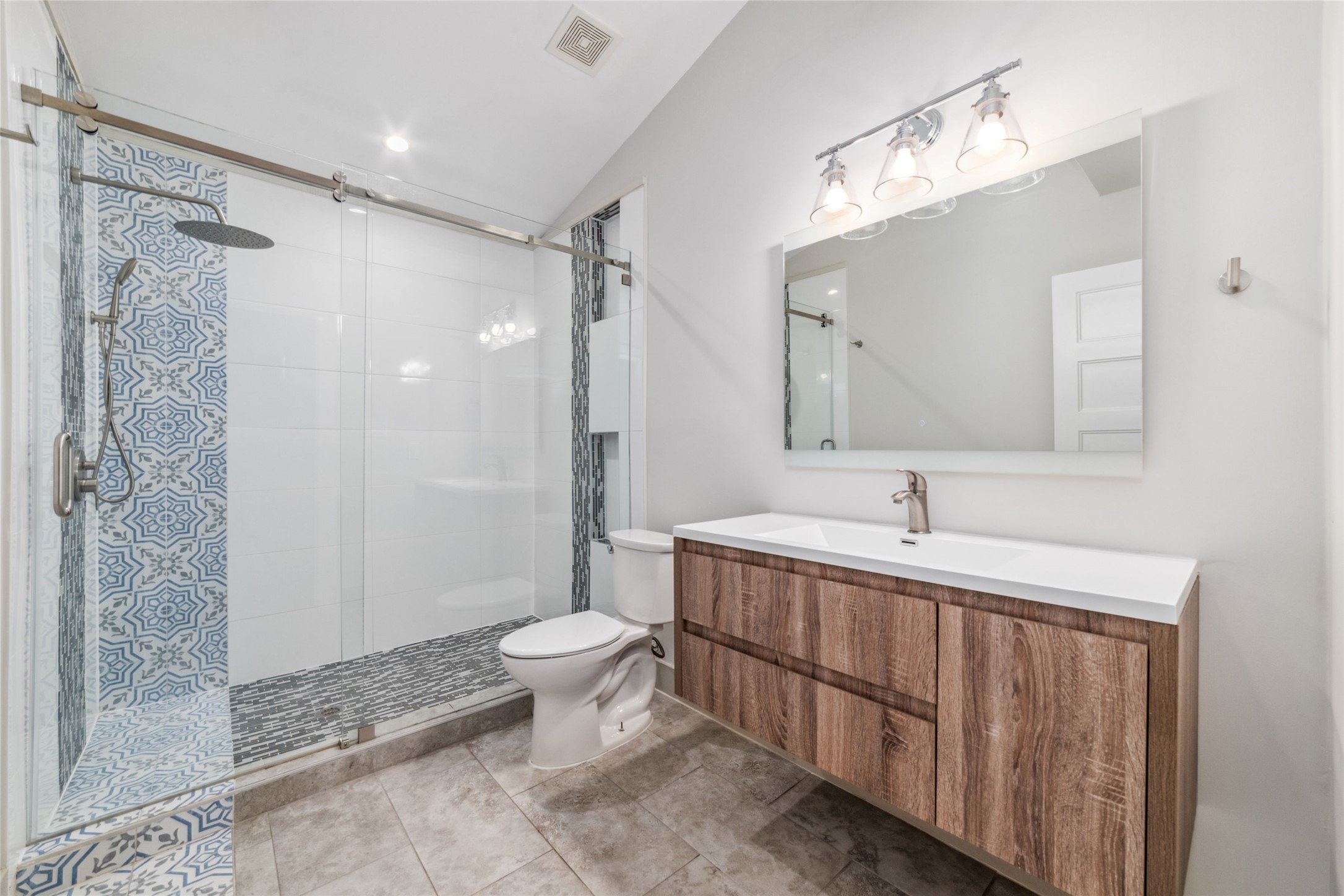9400 Spring Branch Drive Houston, TX 77080 - Photo 20 of 45 Modern bathroom featuring a spacious walk-in shower with stylish blue and white tile accents, a sleek wood vanity with ample storage, and bright overhead lighting for a clean, contemporary look.
