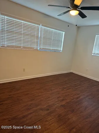 an empty room with wooden floor fan and windows