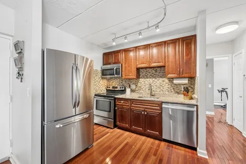 a kitchen with stainless steel appliances granite countertop a refrigerator a sink dishwasher a stove and white countertops with wooden floor