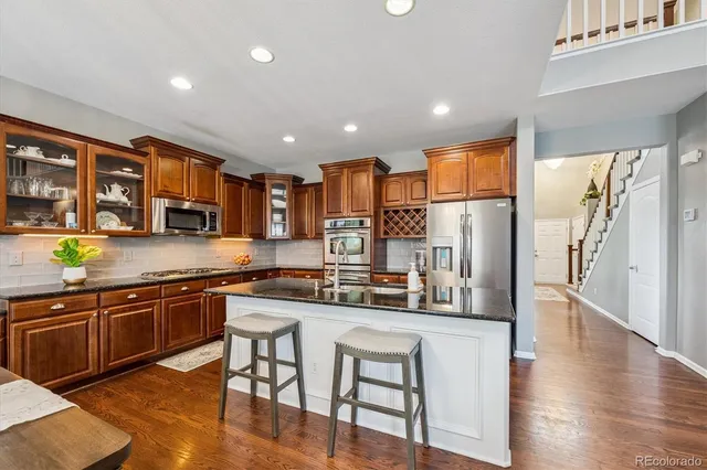 a kitchen with stainless steel appliances granite countertop a stove top oven a refrigerator a sink and dishwasher with wooden floor