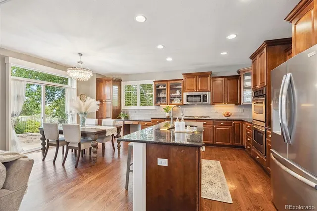 a kitchen with stainless steel appliances granite countertop a stove top oven a sink dishwasher a dining table and chairs with wooden floor