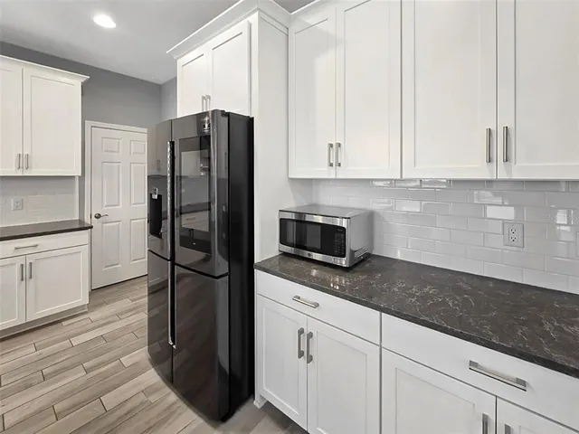 a kitchen with granite countertop a refrigerator a stove and white cabinets with wooden floor