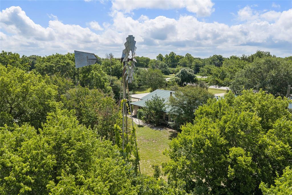 440 Williams Road Lorena, TX 76655 - Photo 11 of 19 Property surrounded by mature trees, featuring a metal windmill and a house with a green roof