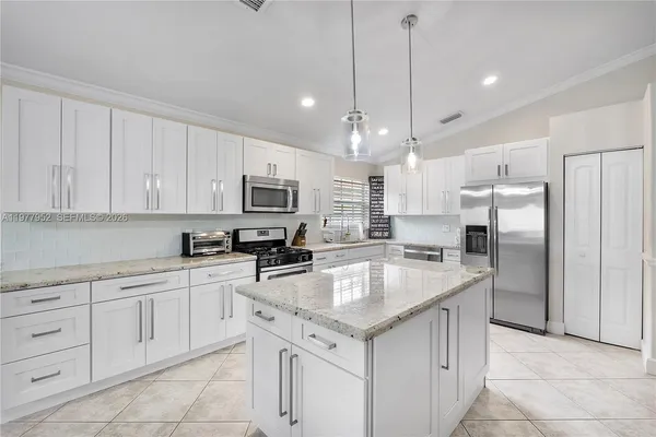 a kitchen with kitchen island granite countertop white cabinets refrigerator and microwave