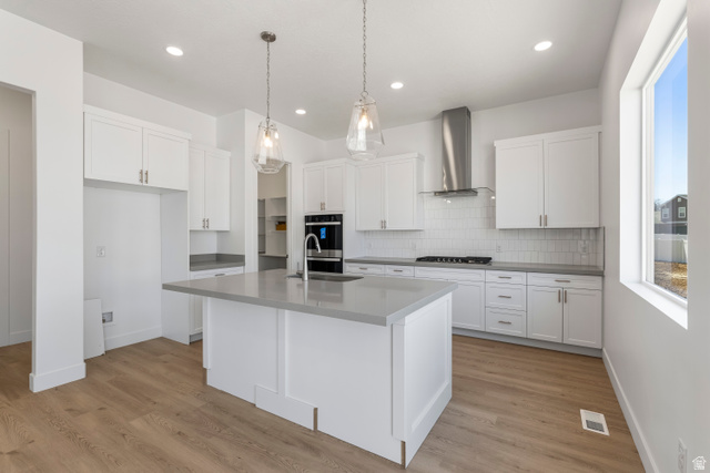 58 South Crimson Way, Unit 306 Mapleton, UT 84664 - Photo 9 of 24 Modern kitchen featuring a central island with a sink, white shaker cabinetry, light-toned countertops, wood-finish flooring, and pendant lighting