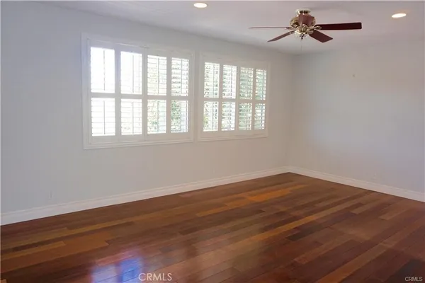 an empty room with wooden floor fan and windows
