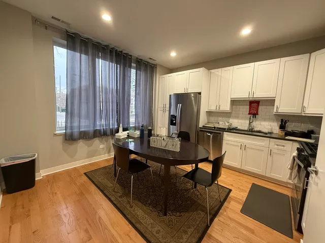 a kitchen with stainless steel appliances granite countertop a stove a refrigerator a sink dishwasher a dining table and chairs with wooden floor