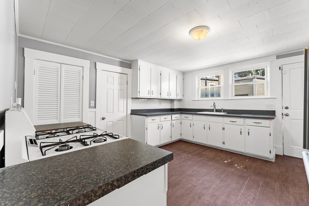 a kitchen with granite countertop a stove a sink dishwasher and white cabinets with wooden floor
