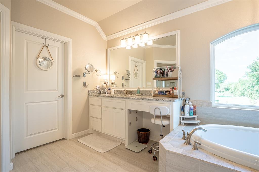 1920 Meander Road Granbury, TX 76049 - Photo 19 of 40 Spacious bathroom featuring a built-in soaking tub with stone tile surround, a large arched window, a double vanity with stone countertop, and wood-finish flooring