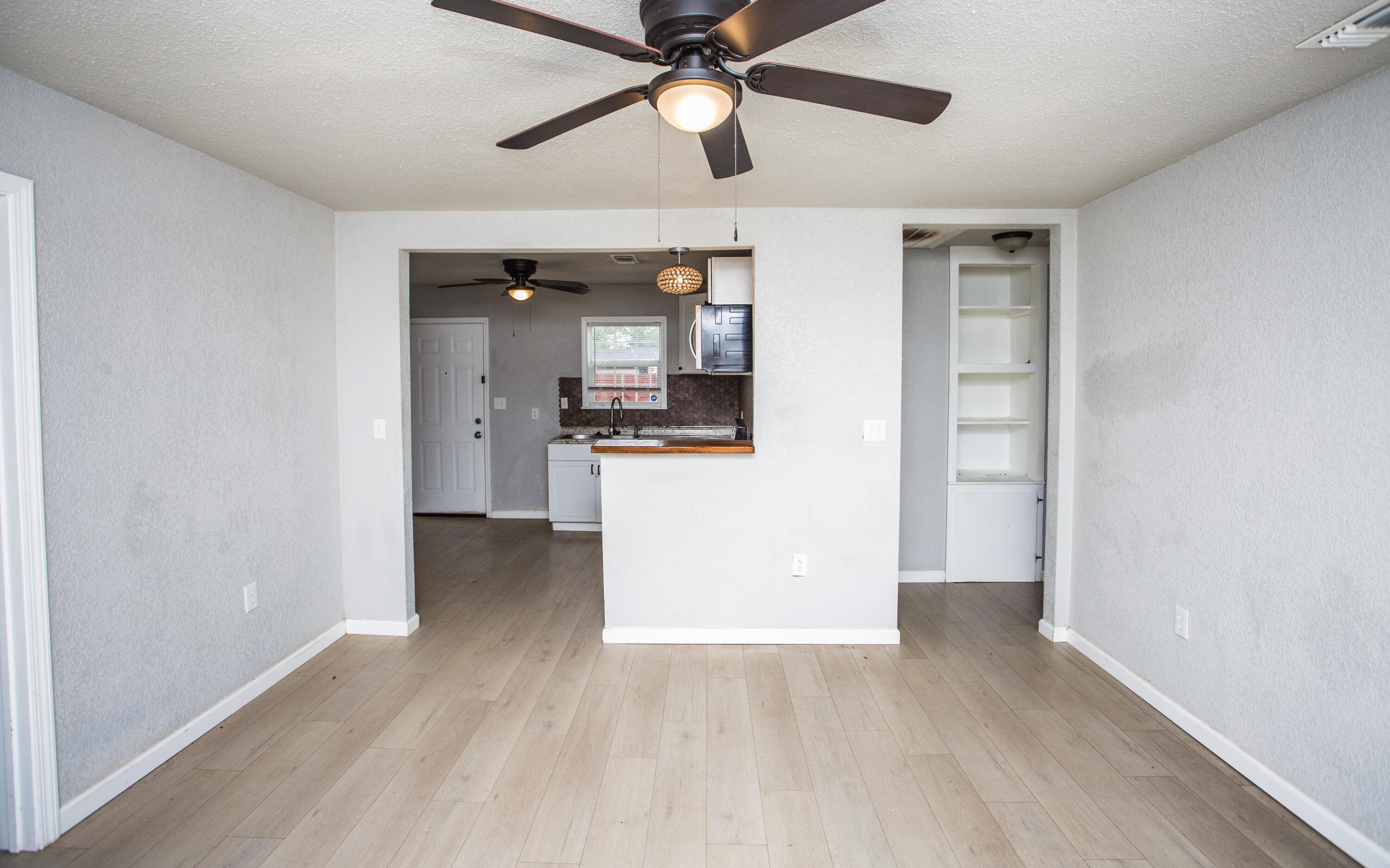 1518 40th Street Lubbock, TX 79412 - Photo 3 of 13 an empty room with wooden floor a ceiling fan and kitchen view
