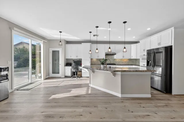 a kitchen with stainless steel appliances granite countertop a refrigerator oven a sink dishwasher and white cabinets with wooden floor