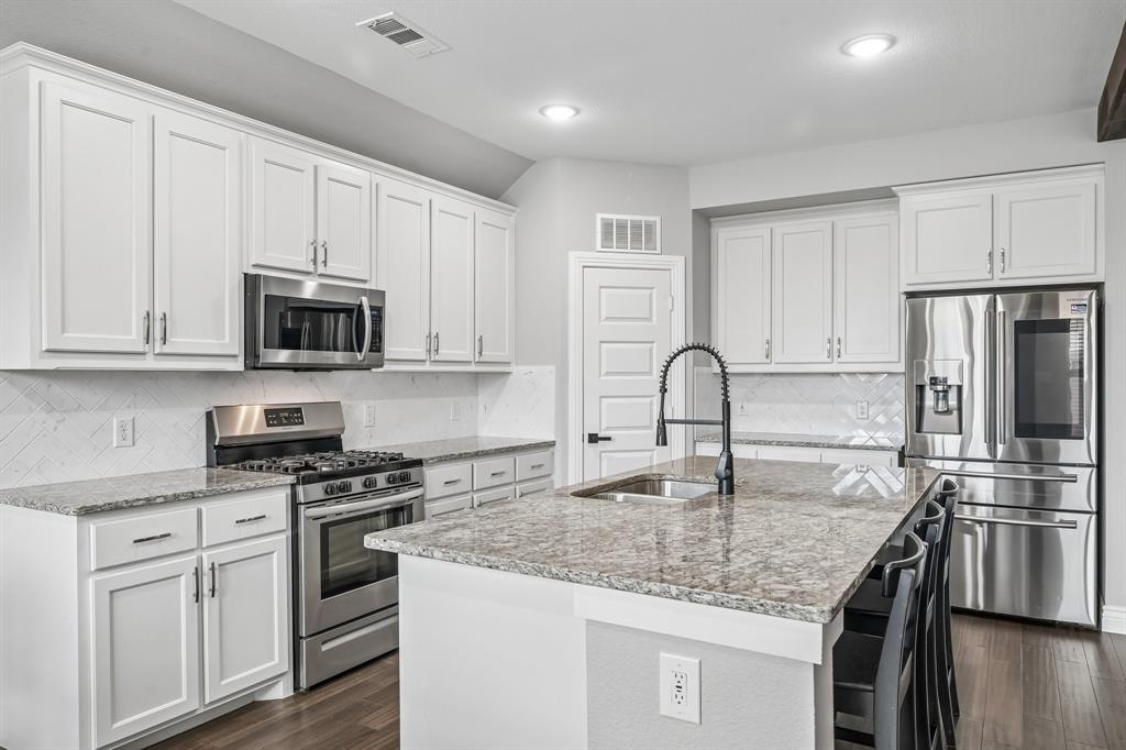 1805 Huntsman Way Forney, TX 75126 - Photo 8 of 34 Modern kitchen featuring an expansive center island with seating, granite countertops, white cabinetry, a black pull-down faucet, and stainless steel appliances