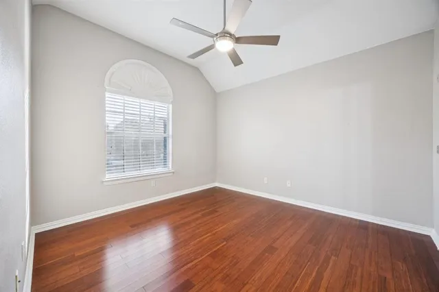 an empty room with wooden floor chandelier fan and windows