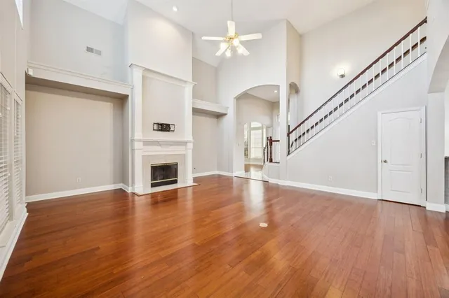 a view of a livingroom with wooden floor a fireplace a ceiling fan and windows