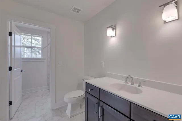 a bathroom with a toilet a sink a mirror and a window