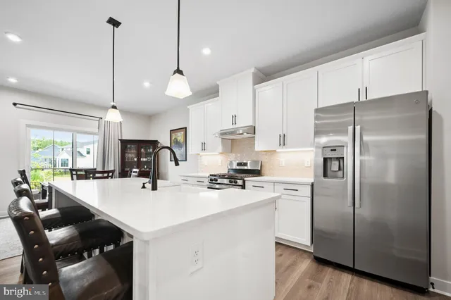 a kitchen with refrigerator a stove a sink dishwasher a dining table and chairs with wooden floor