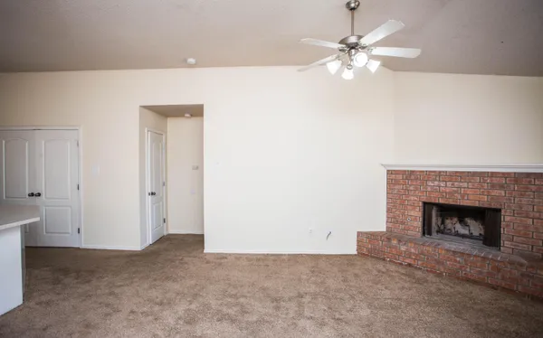 a view of an empty room with chandelier fan and fire place