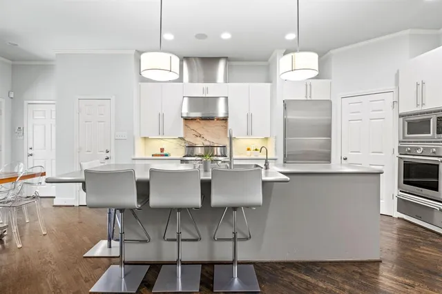 a kitchen with stainless steel appliances kitchen island granite countertop a sink a stove a refrigerator and white cabinets with wooden floor