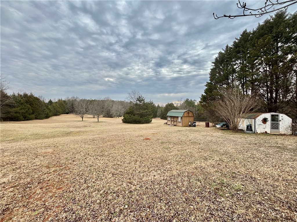 354 Harper Road Pendleton, SC 29670 - Photo 29 of 30 Expansive outdoor area with various structures and mature trees under a vast sky.