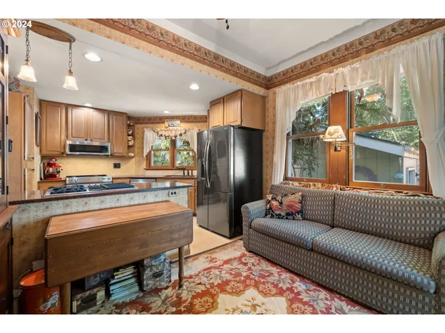 a living room with stainless steel appliances furniture a large window and a kitchen view