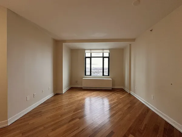 a view of an empty room with wooden floor and window