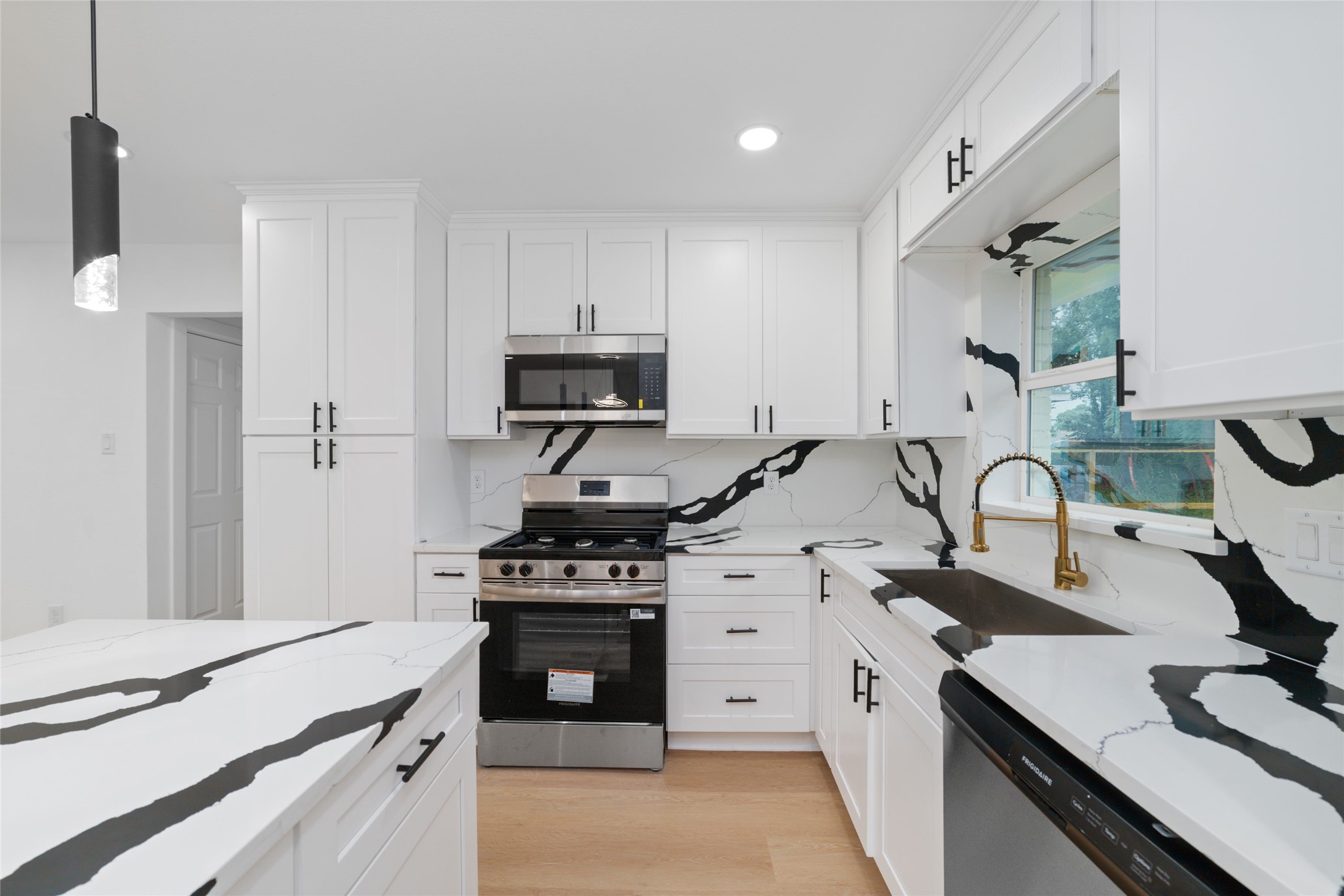 5709 Langley Road Houston, TX 77016 - Photo 8 of 27 This modern kitchen features sleek white cabinetry, striking black and white marble countertops and backsplash, stainless steel appliances, and a contemporary pendant light, creating a bright and stylish space.