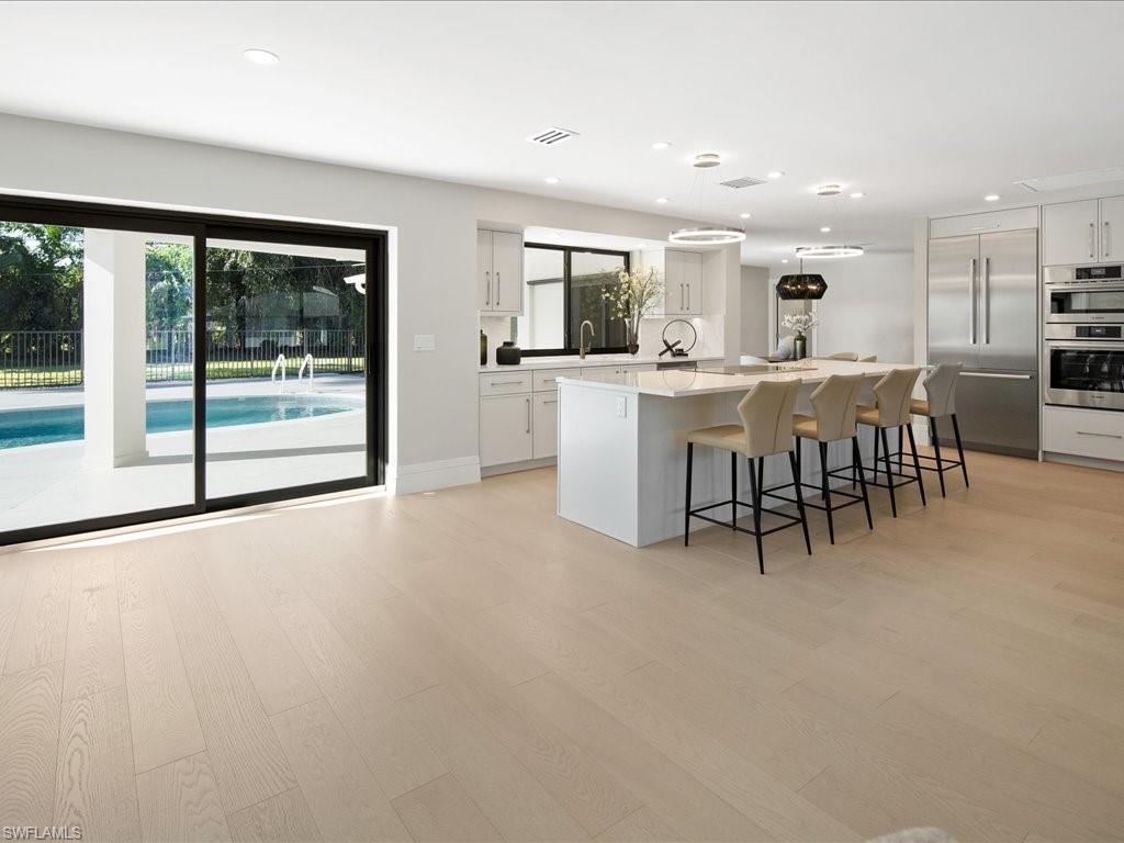 518 Cypress Way East Naples, FL 34110 - Photo 3 of 50 Kitchen featuring white cabinets, light wood-type flooring, appliances with stainless steel finishes, and a center island