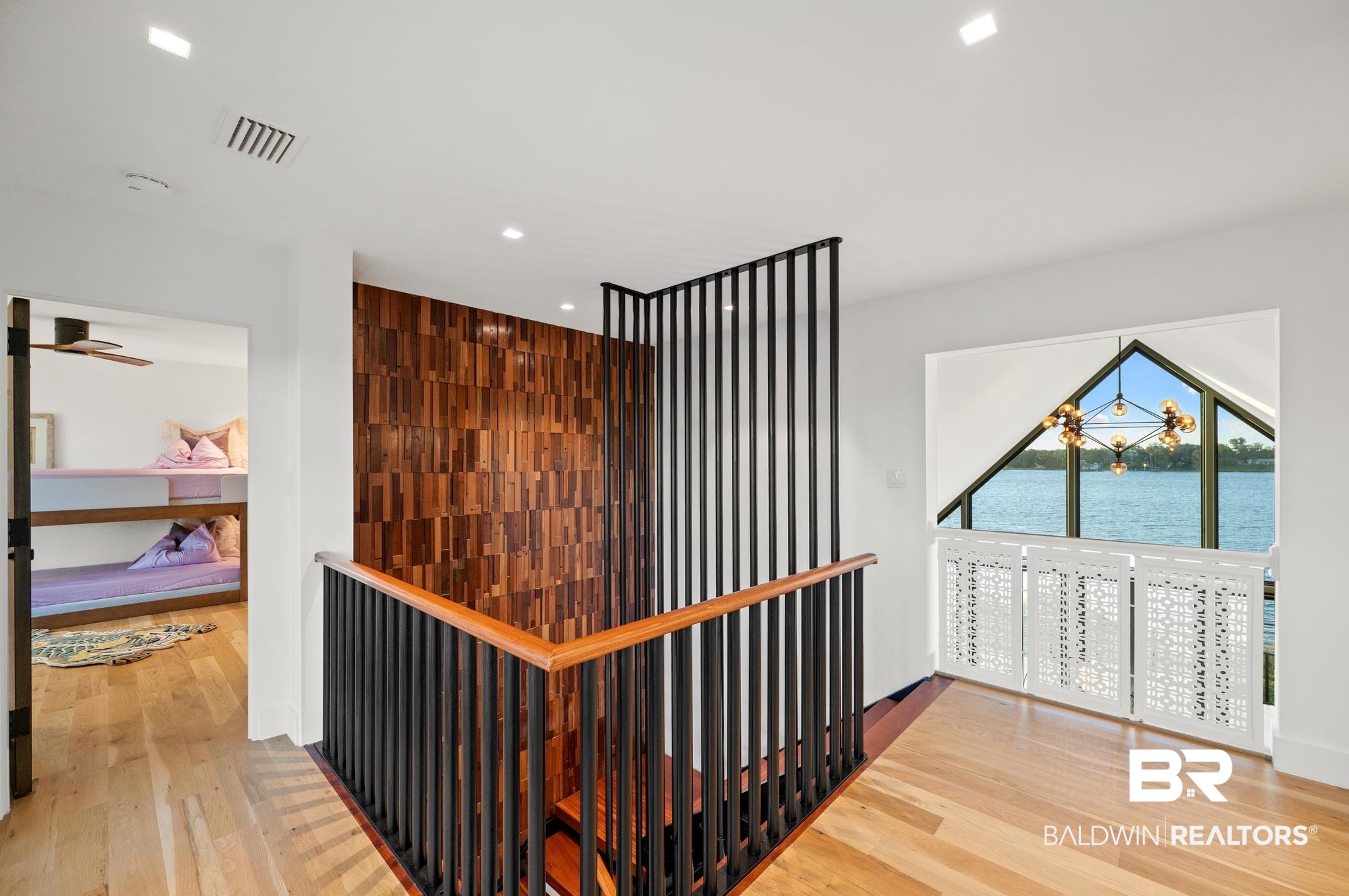 33349 River Road Orange Beach, AL 36561 - Photo 37 of 61 Open landing featuring wood-finish flooring, a contemporary wood accent wall, and a staircase with a black metal and wood railing