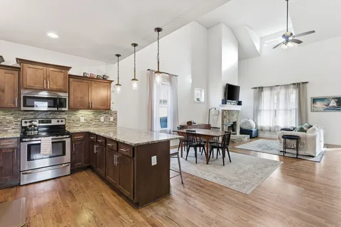 a kitchen with stainless steel appliances granite countertop a stove top oven a refrigerator a dining table and chairs with wooden floor