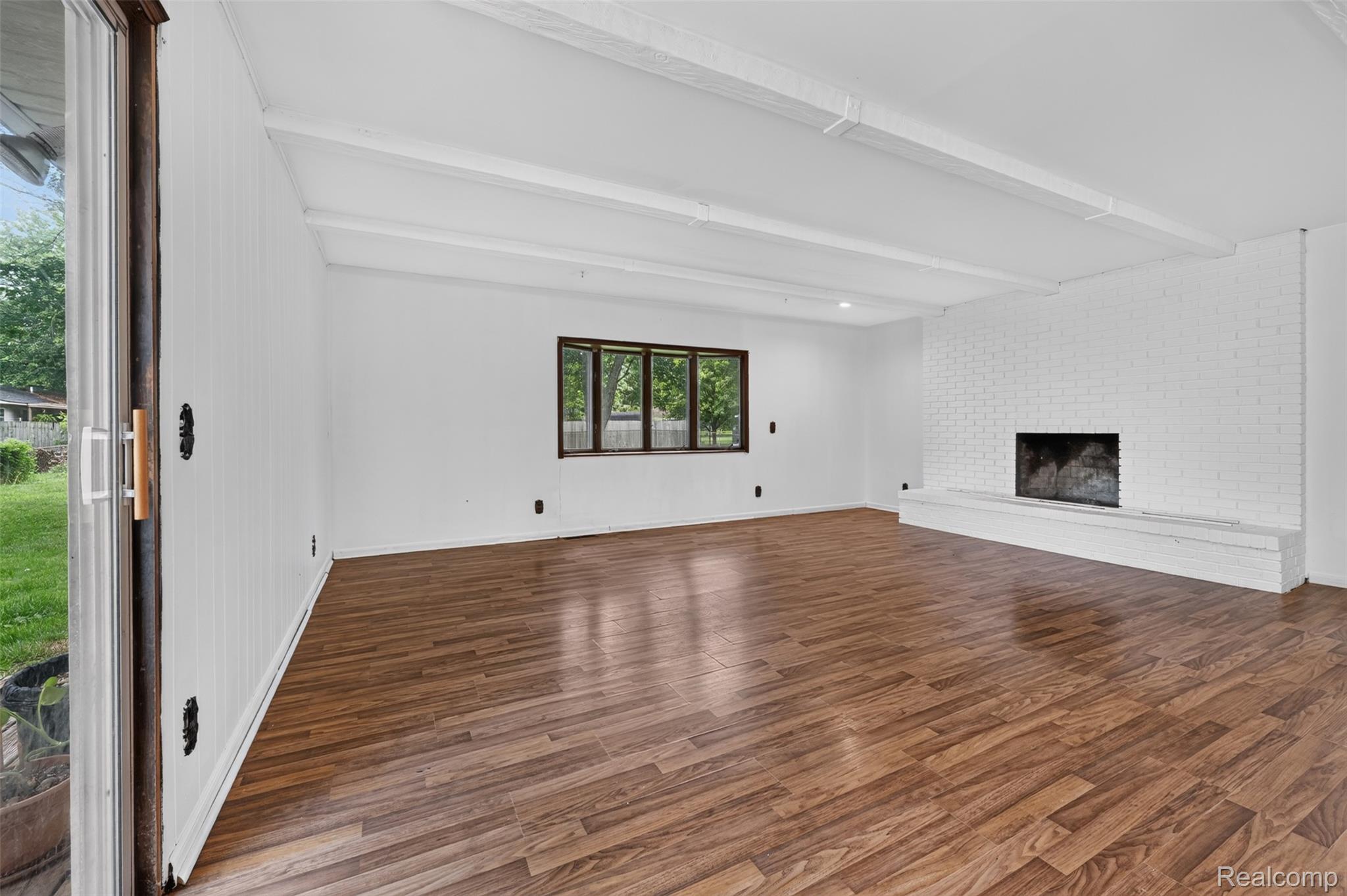 5457 Reid Road Swartz Creek, MI 48473 - Photo 19 of 51 Spacious room featuring wood-finish flooring, a painted brick fireplace, exposed white ceiling beams, and a large window