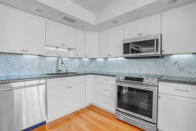 a kitchen with granite countertop white cabinets stainless steel appliances and wooden floor