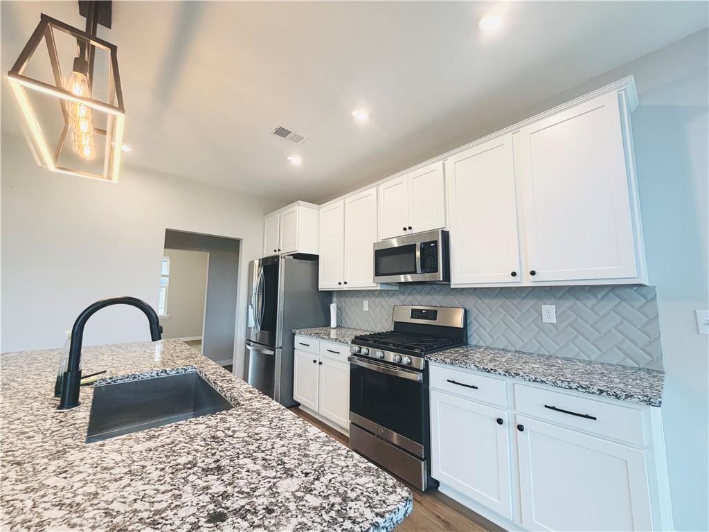 607 Michigan Circle Hoschton, GA 30548 - Photo 6 of 27 a kitchen with stainless steel appliances granite countertop a stove a sink a refrigerator and white cabinets with wooden floor