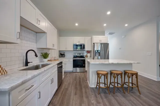 a kitchen with stainless steel appliances granite countertop a refrigerator a sink a stove a dining table and chairs with wooden floor