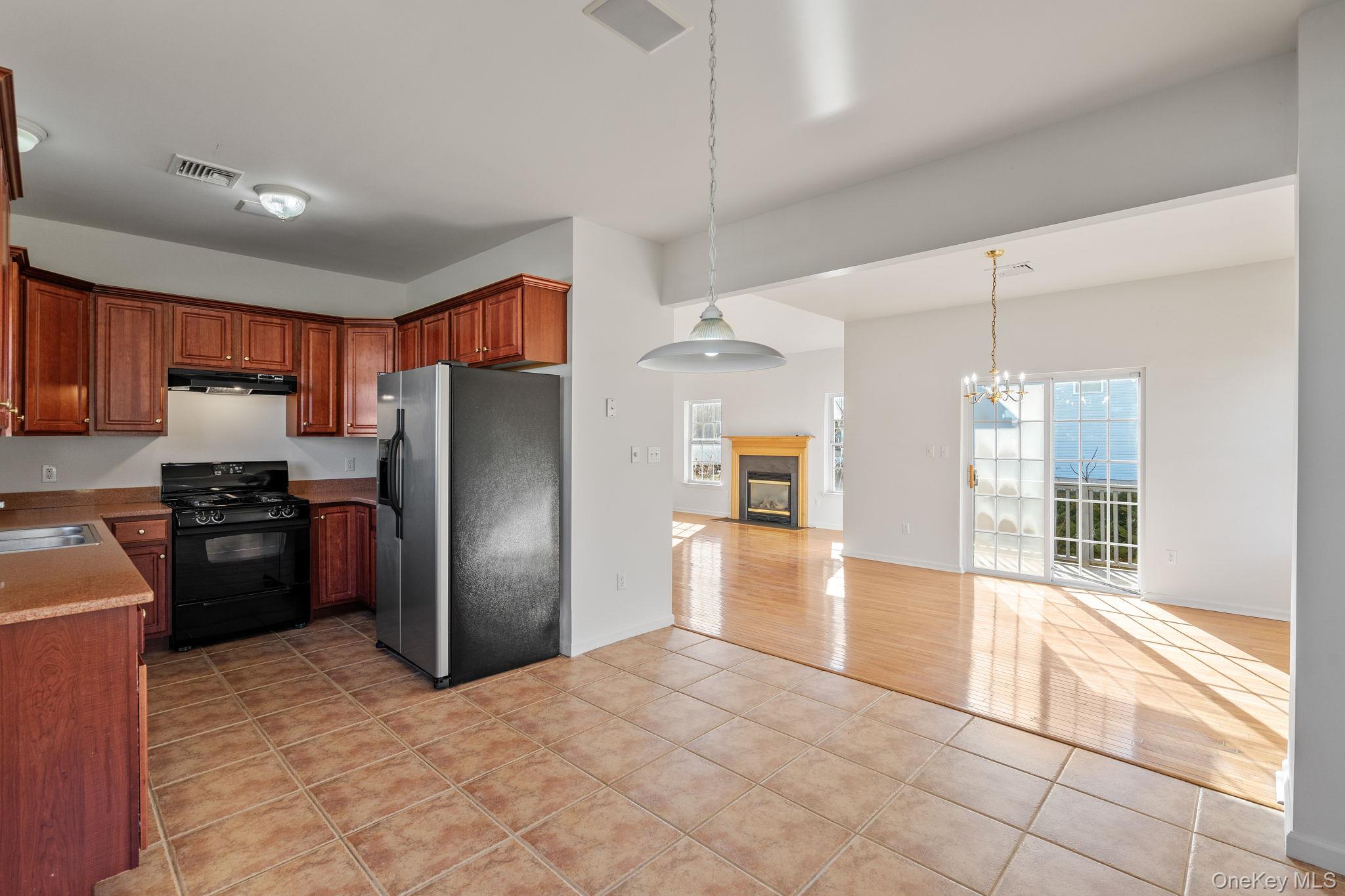 17 Carmella Road Highland, NY 12528 - Photo 15 of 48 Kitchen featuring stainless steel refrigerator with ice dispenser, black range with gas stovetop, a glass covered fireplace, light tile patterned floors, and decorative light fixtures