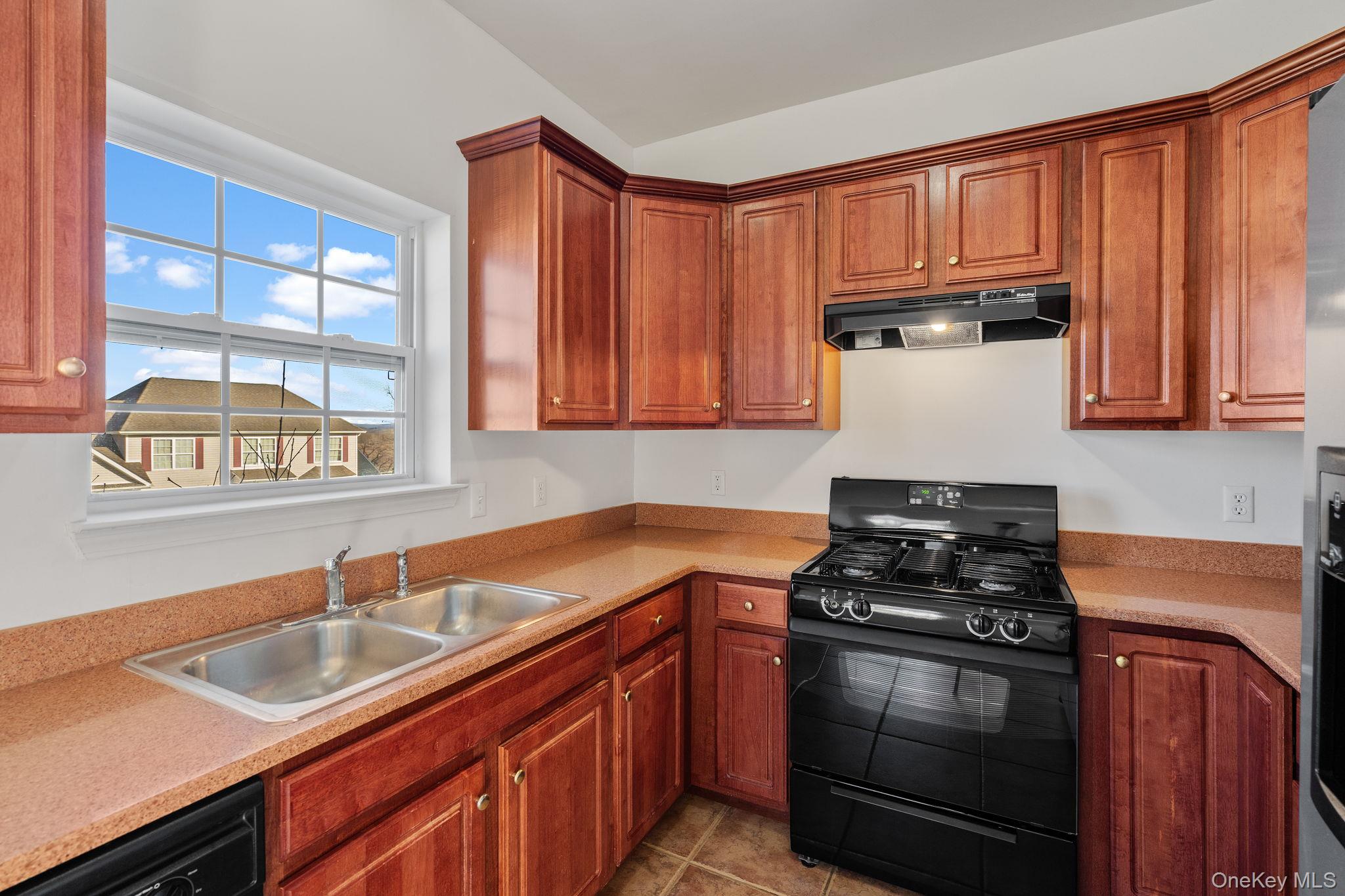 17 Carmella Road Highland, NY 12528 - Photo 17 of 48 Kitchen with black appliances, under cabinet range hood, brown cabinets, light tile patterned flooring, and light stone counters