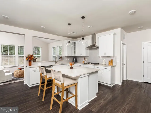 a view of a kitchen with kitchen island a stove a sink dishwasher a oven with a dining table and chairs with wooden floor