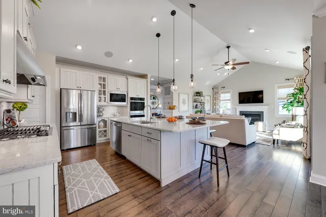 a kitchen with stainless steel appliances kitchen island a refrigerator a stove a oven a sink dishwasher and white cabinets with wooden floor