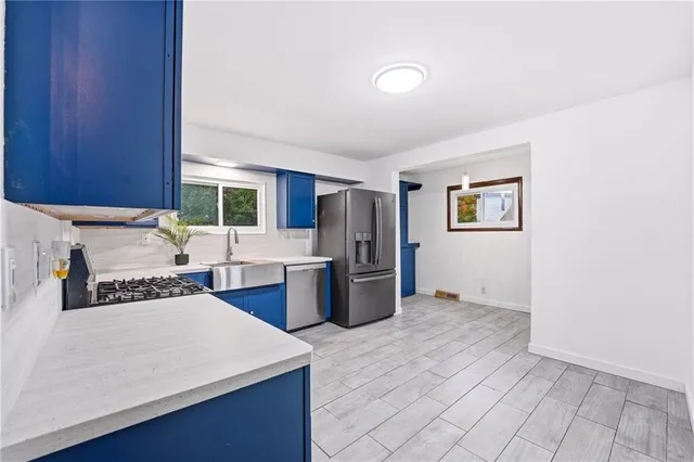 a kitchen with stainless steel appliances a stove a sink a refrigerator white cabinets and wooden floor