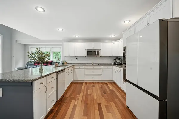 a large white kitchen with stainless steel appliances granite countertop a refrigerator sink and white cabinets