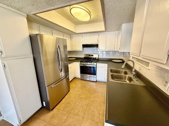 a kitchen with stainless steel appliances granite countertop a refrigerator a stove and a sink with wooden floor