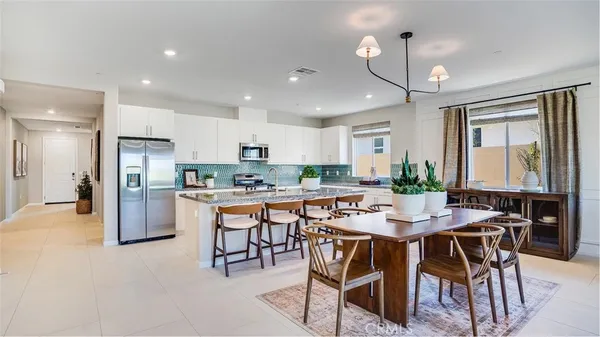 a kitchen with stainless steel appliances kitchen island granite countertop a dining table chairs refrigerator and microwave